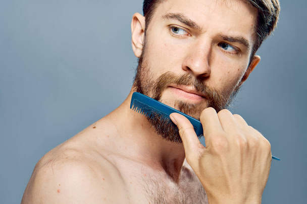 Un hombre con un peine en sus manos cuidando una barba hombros desnudos  - Foto, imagen