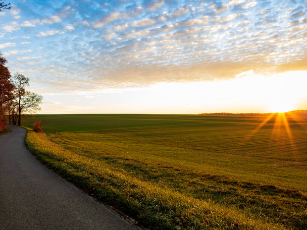 Un plan en angle élevé d'une route par une belle prairie couverte d'herbe capturée au coucher du soleil - Photo, image