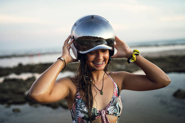 A shallow focus of a cheerful female posing with a helmet at the beach of Chiclana, Spain - Фото, изображение