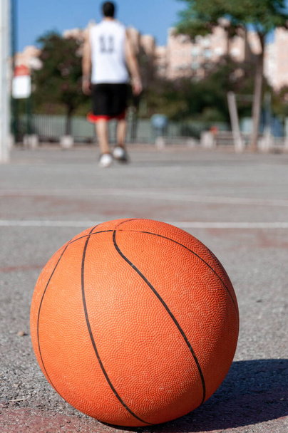 A vertical selective focus shot of a basketball ball in a court and a person in the background - Photo, Image