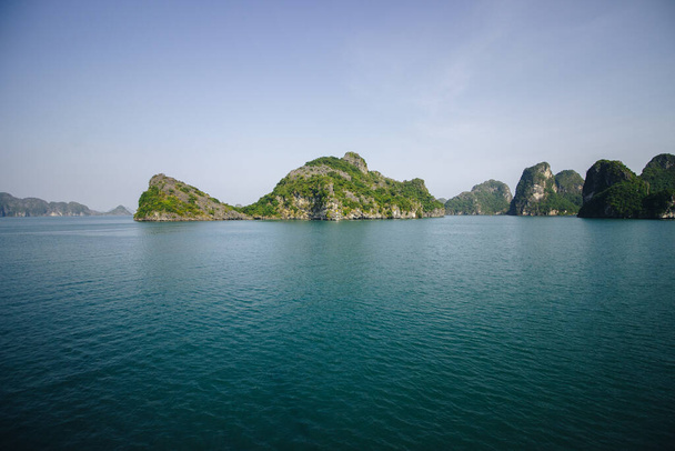 The limestone islands topped by trees and their reflection on the turquoise water of Ha Long Bay in Vietnam - Фото, изображение