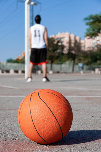 A vertical selective focus shot of a basketball ball in a court and a person in the background - Photo, Image