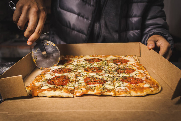 A closeup shot of a person cutting a homemade pizza on a cardboard box - Foto, afbeelding