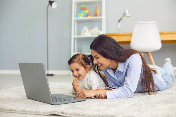 gelukkig moeder en haar schattig dochtertje kijken online entertainment video samen op laptop thuis - Foto, afbeelding