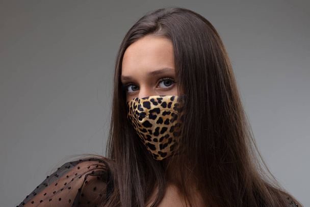 Donna che indossa un'elegante maschera protettiva per il viso con motivo a stampa animale come controllo delle infezioni contro il coronavirus durante la pandemia di Covid-19 nel look New Normal su grigio - Foto, immagini