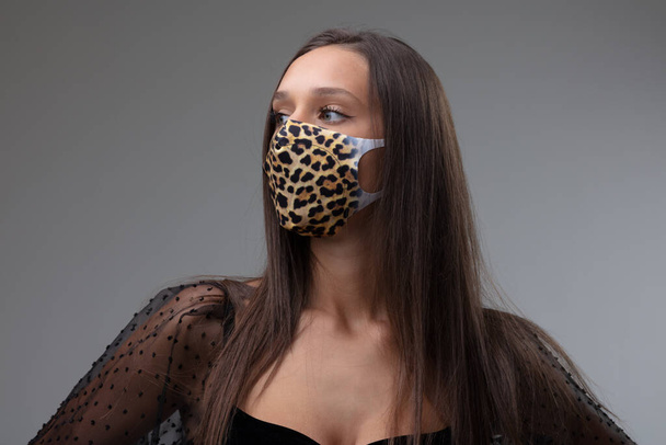 Vrouw met een textielmotief masker met dierenprint tijdens de Covid-19 pandemie als bescherming tegen coronavirus naar de zijkant kijkend in een stijlvol zwart topje - Foto, afbeelding
