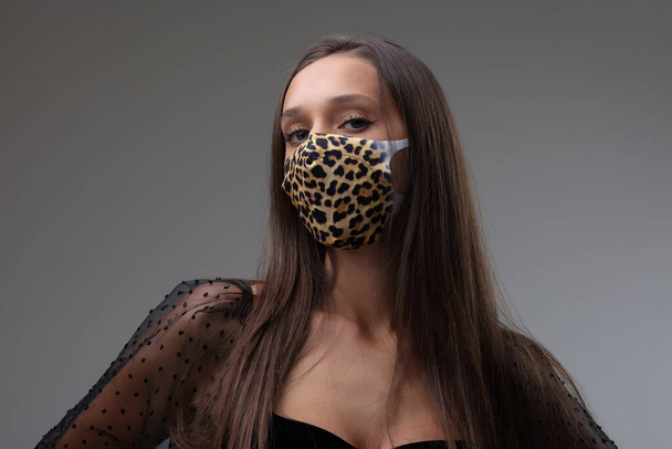 Nuori brunette nainen yllään tyylikäs kasvonaamio eläinten tulostaa kuvio suojana aikana Covid-19 pandemia käsite New Normal lifestyle vastaan harmaa tausta - Valokuva, kuva