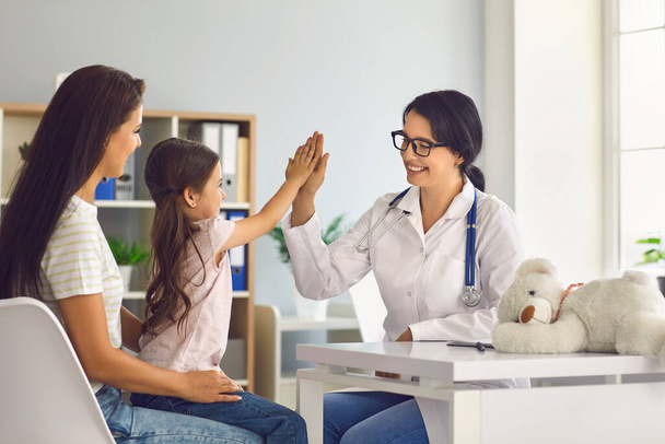 Женщина-врач дает пять рук маленькой девочке на консультации в клинике. - Фото, изображение