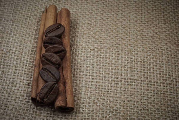 Granos de café tostados en barras de canela con fondo de arpillera desde la vista lateral superior - Foto, Imagen