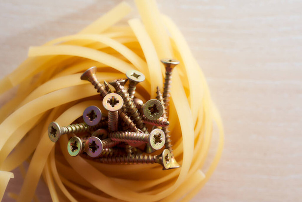 The screws lie in the nest of spaghetti light background. High quality photo - Photo, Image