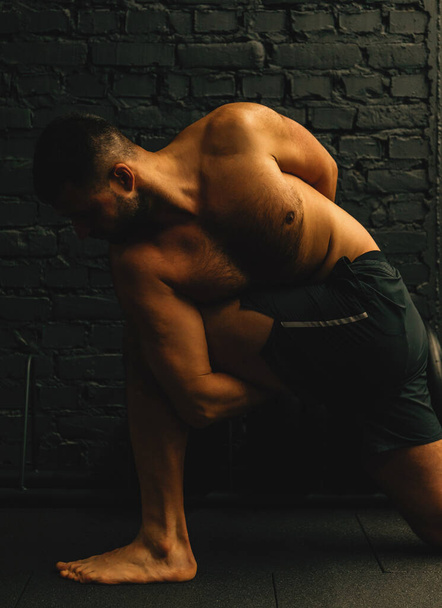Atrakcyjny mężczyzna w średnim wieku ćwiczący jogę, siedzący w trudnej pozycji, ćwiczący w czarnej odzieży sportowej. Koncepcja zdrowego stylu życia. - Zdjęcie, obraz