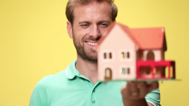 glücklicher junger, lässiger Mann, der das Haus anschaut und lächelt, auf gelbem Hintergrund stehend - Filmmaterial, Video