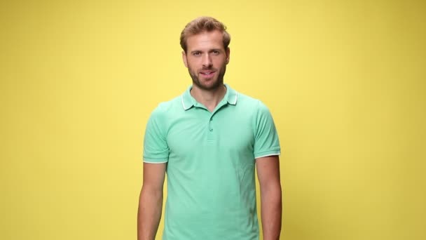 casual young model smiling, holding hands in pockets, looking up and making thumbs up gesture on yellow background - Footage, Video