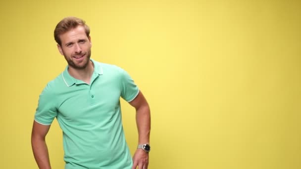 young casual guy holding hands on hips and moving, smiling, crossing arms and standing on yellow background - Footage, Video