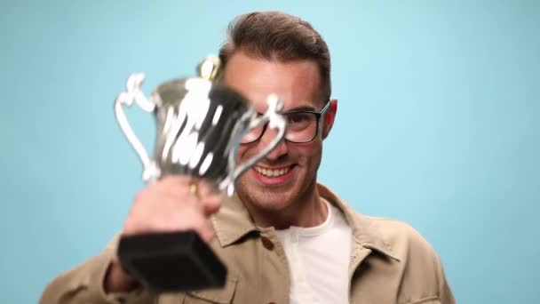 jonge casual man met zijn trofee dan het verhogen van het samen met zijn vuist en vieren succes op blauwe achtergrond - Video