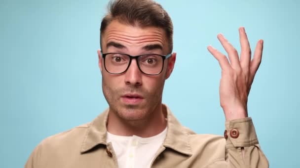 young casual guy fixing his glasses and being took by surprise, scratching his head and then finding a solution on blue background - Footage, Video