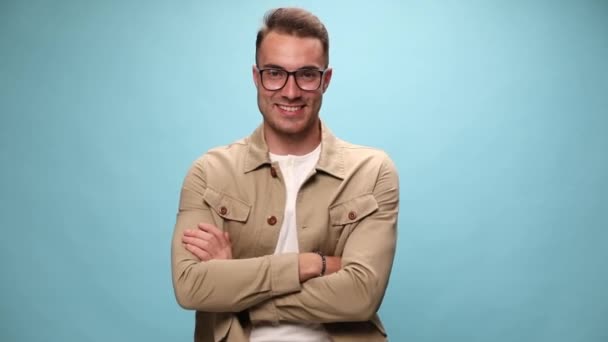 sexy lässiger Kerl verschränkt seine Arme mit einem Lächeln im Gesicht und zeigt auf die Kamera auf blauem Hintergrund - Filmmaterial, Video