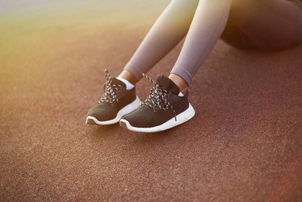 Benen van een zwart meisje in sport leggings en sneakers op een sportveld op straat. - Foto, afbeelding