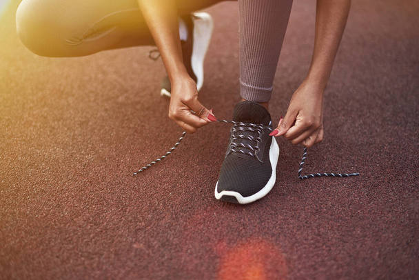 Black girl laces up her sneakers while doing sports on the street. Outdoor fitness concept. - Foto, Imagem