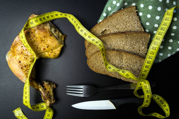 Pişmiş tavuk budu, çavdar ekmeği, çatal ve bıçak. Siyah arkaplanda üst görünüm - Fotoğraf, Görsel