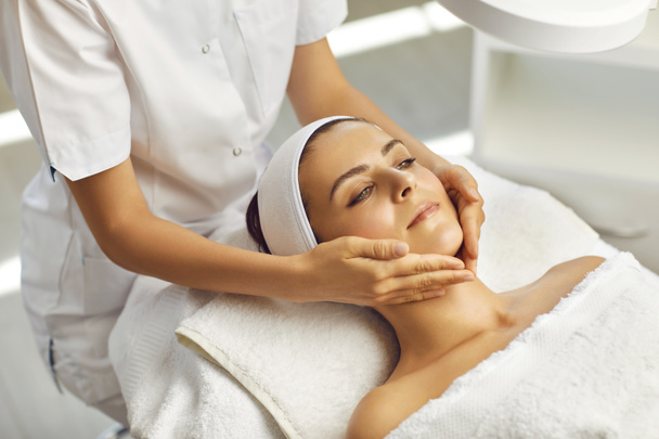 Hands of cosmetologist massaging relaxed womans face in spa beauty salon - Foto, Imagem