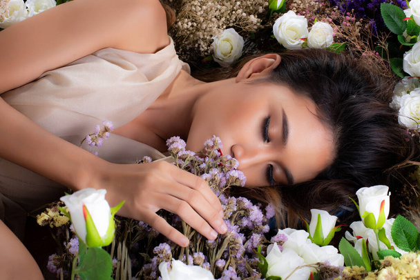 Retrato de moda 20s mujer asiática tiene hermosa actualización maquillaje artista en cepillo y lápiz labial rojo, ella se acuesta dormir en flor de arbusto de muchos tipos de campo de flores, espacio de copia - Foto, imagen