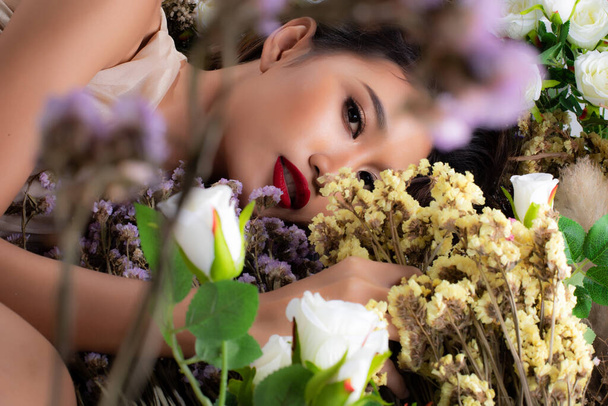 Portret van Fashion 20s Aziatische vrouw heeft mooie update make-up kunstenaar op borstel en rode lippenstift, ze liggen slapen in bush bloesem van vele soorten Flower veld, kopieer ruimte - Foto, afbeelding