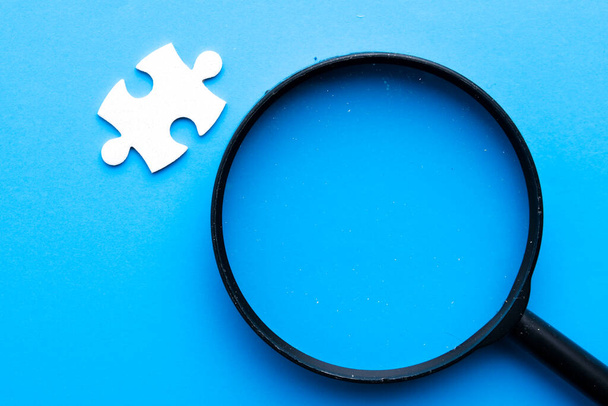 Μια εικόνα μεγεθυντικού φακού με ένα κομμάτι παζλ σε μπλε φόντο. Κάθε πρόβλημα έχει τη λύση του έννοια. - Φωτογραφία, εικόνα