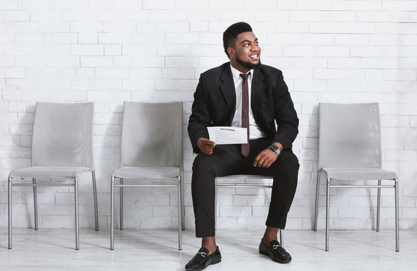 Felice ragazzo nero in abito da lavoro in attesa di colloquio di lavoro presso la sala aziendale, spazio vuoto - Foto, immagini