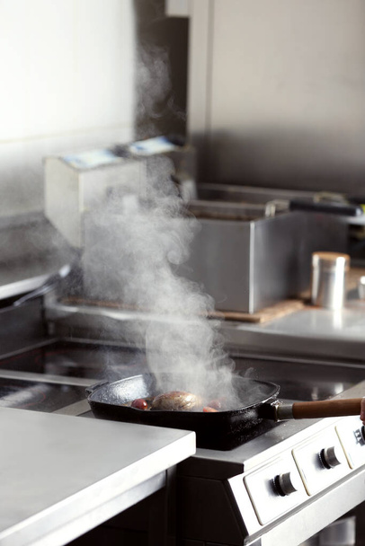 Cooking delicious meat on frying pan in restaurant kitchen - Foto, afbeelding