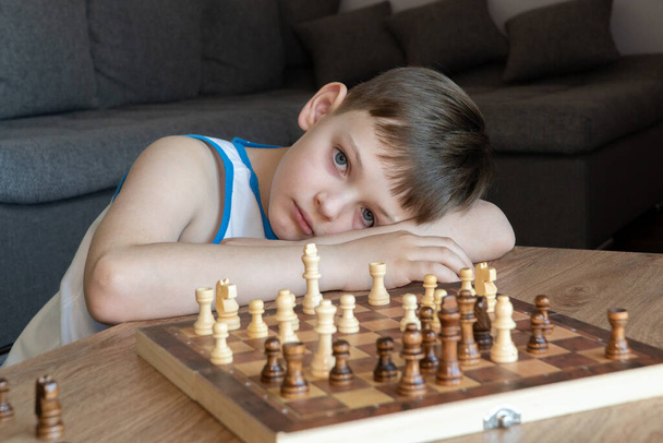 Серьезный ребенок, потерявшийся в мыслях, играя в шахматы. Играл в настольные игры, на карантине коронавируса. Ребенок играет в шахматы. - Фото, изображение