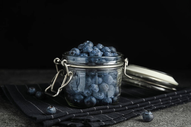 Tasty ripe blueberries in glass jar on grey table - Photo, image
