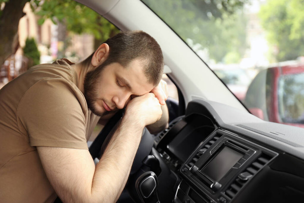 Tired man sleeping on steering wheel in his car - Foto, afbeelding