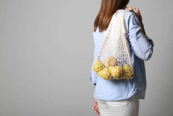 Woman holding net bag with fresh ripe pears on grey background, closeup. Space for text - Foto, afbeelding