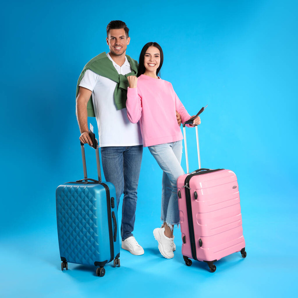 Happy couple with suitcases and tickets in passports for summer trip on blue background. Vacation travel - Photo, Image