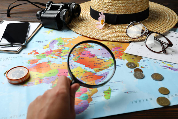 Woman looking through magnifying glass on world map at table, closeup. Travel during summer vacation - Фото, зображення