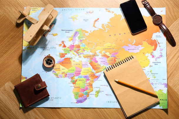 Плоская композиция с картой мира и различными предметами на деревянном фоне. Планирование поездок - Фото, изображение