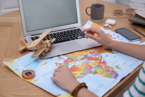 Woman with world map and laptop planning trip at wooden table, closeup - Photo, Image