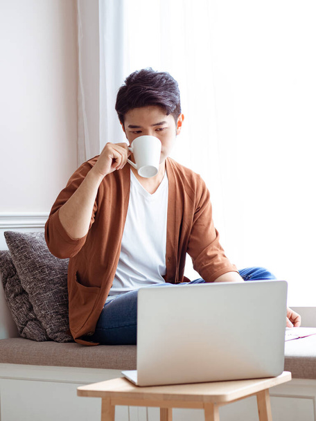 Aziatische jongeman zitten aan de tafel in de voorkant van laptop computer - Foto, afbeelding