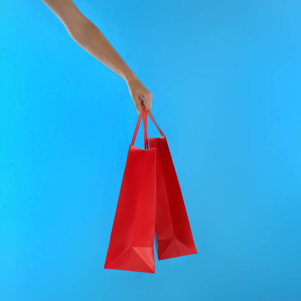 Woman with paper shopping bags on light blue background, closeup - Foto, Bild