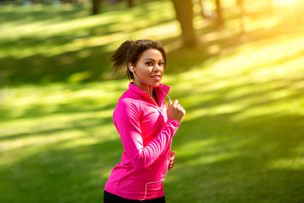 Pretty african girl running by park, listening to music - Photo, Image