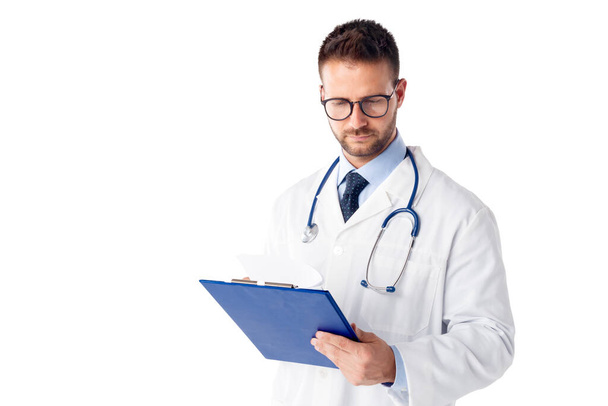 Studio shot of male doctor holding clipboard in his hand while standing at isolated white background. Copy space. - Φωτογραφία, εικόνα