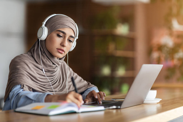 Mädchen mit Kopftuch bei Online-Unterricht auf Laptop im Café - Foto, Bild