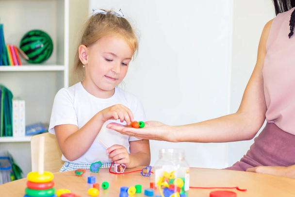 developmental and speech therapy classes with a child-girl. Speech therapy exercises and games with beads. The girl has beads in her hands - Foto, imagen
