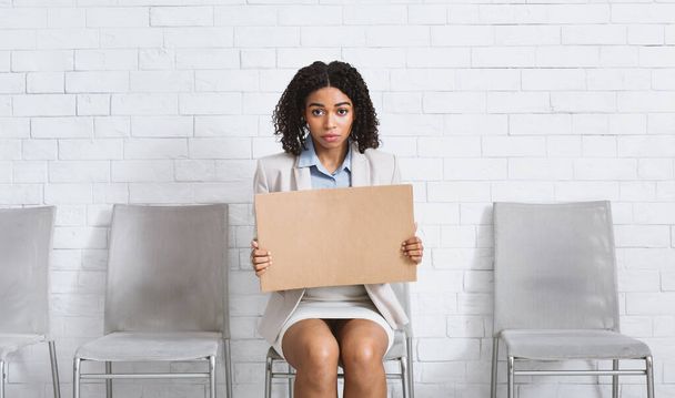 Jeune femme noire avec panneau vierge en attente d'une entrevue d'emploi dans le hall du bureau, espace pour le design - Photo, image