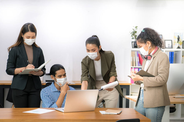 Asian office workers wearing face masks working in new normal office and doing social distancing during corona virus covid-19 pandemic - Foto, Imagem