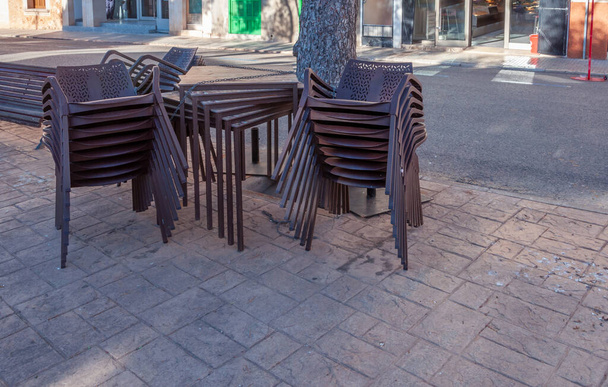 Cadeiras de plástico marrom empilhadas ao lado de mesas ao ar livre. Restaurante fechado por Coronavirus
 - Foto, Imagem