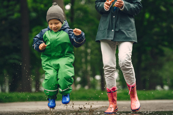 Funny kid in rain boots playing in a rain park - Foto, Imagem
