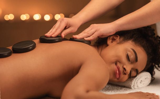 Massaggio curativo con pietre calde per una donna nera gioiosa - Foto, immagini