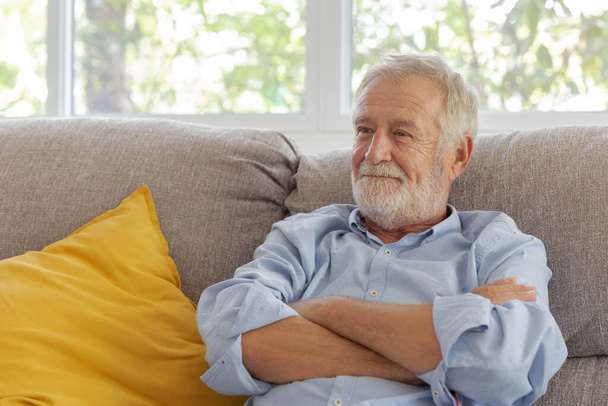 Счастливый пенсионер улыбается, сидя дома на диване. - Фото, изображение
